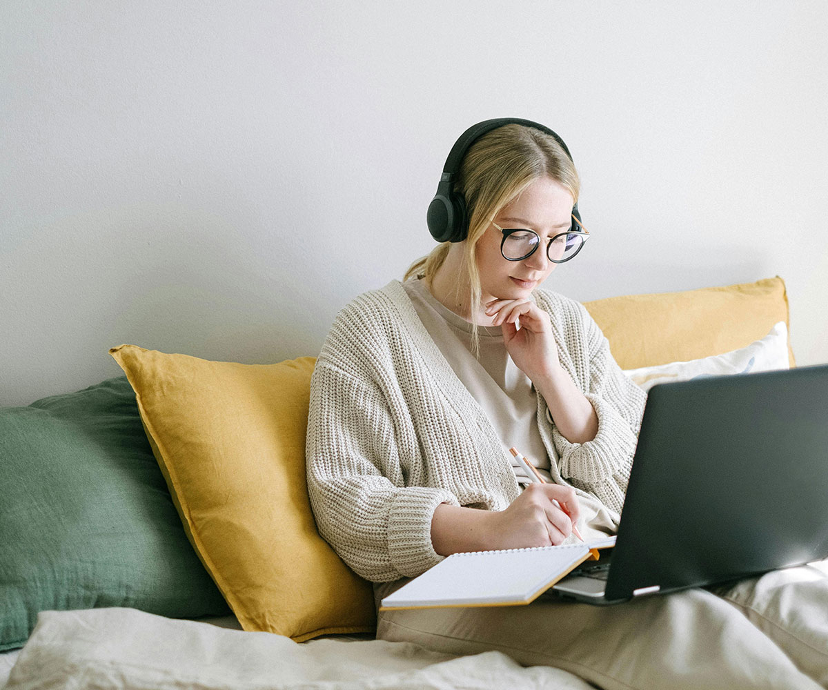 A women studying on her laptop with headphones on.